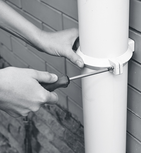 Worker Installing rain gutter downpipe. Contractor hands repair rain gutter downspout pipe with screwdriver. Guttering, Gutters, Plastic Guttering, Guttering & Drainage. Guttering Down pipe Fittings